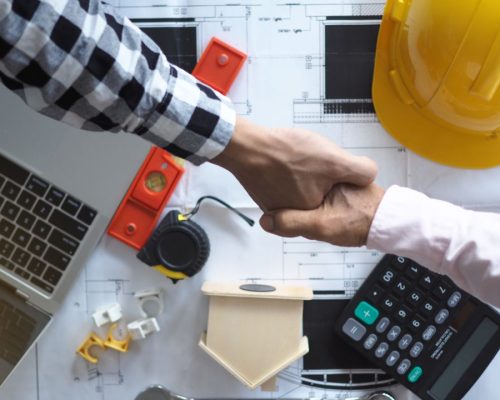 Top view of a handshake above a calculator, floor plans, and construction tools.